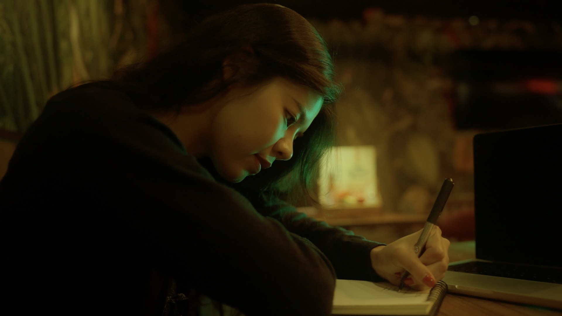 Graded frame: woman writing in a notebook in moody green and amber light