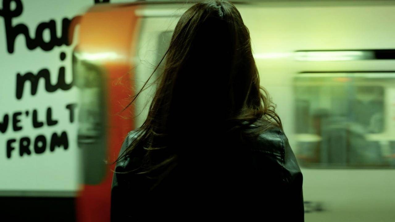 A woman with long hair watching a train rush past on an Underground platform