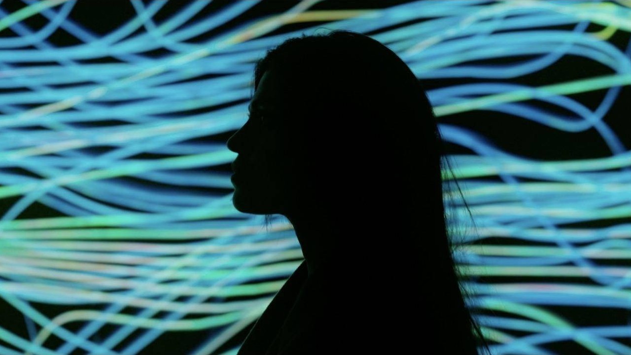 Silhouette of a woman in profile against glowing blue and green light trails